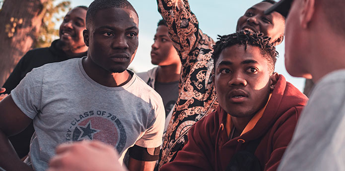 A gathering of people. Two black men in the foreground talk with a white guy.