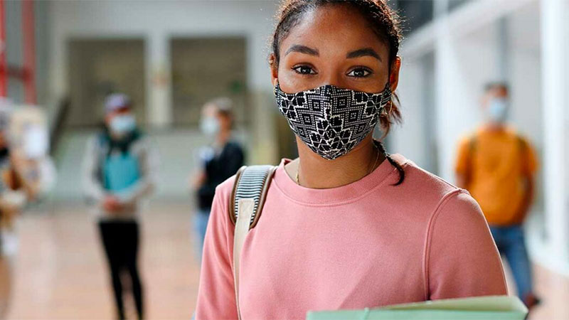 Black female student wearing a COVID mask, pink sweatshirt, carrying a backpack.