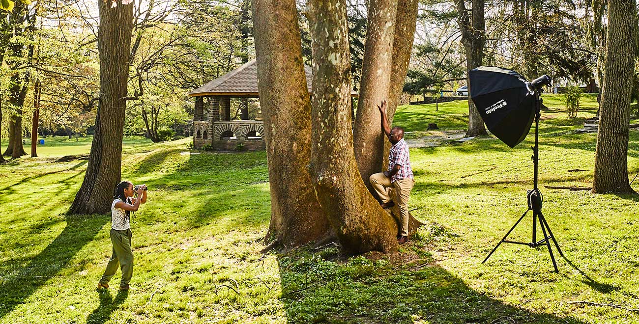 Dee taking a photo of her father by a tree in a park.