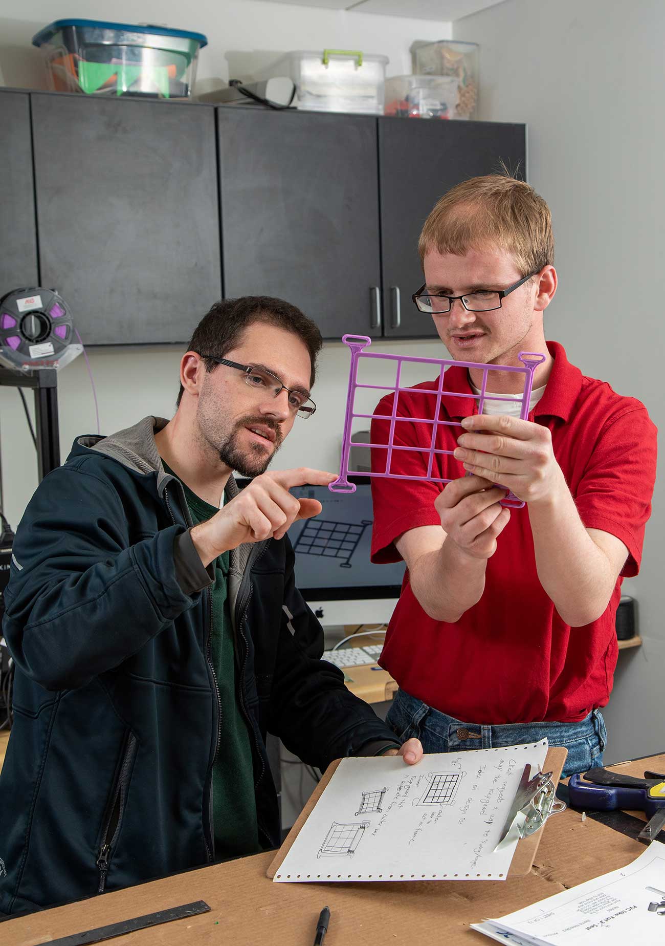 Student Trevor Larsen holds up a magenta 3d printed part for inspection.