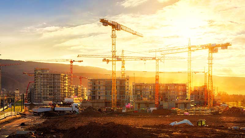 Long shot of cranes constructing highrise buildings with an orange sunset behind them.