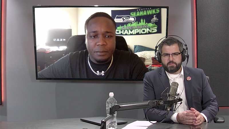 Podcast host Dakota Pawlicki with headphones and microphone on the set during the podcast recording with guest on the screen behind him.