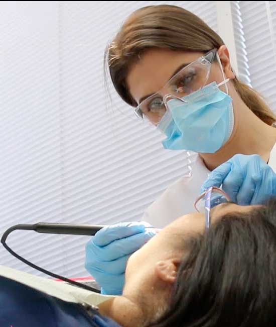 Dental Hygienist in blue mask gloves and mask holding a dental implement inside someone's mouth.