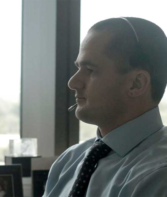 Man in high rise office wearing tie and telecommunication headset.