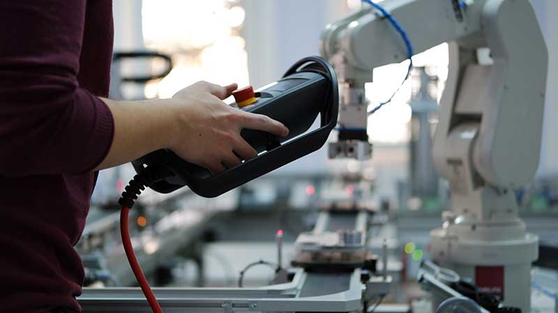 Stock photo of a human controlling a robot with a handheld remote.