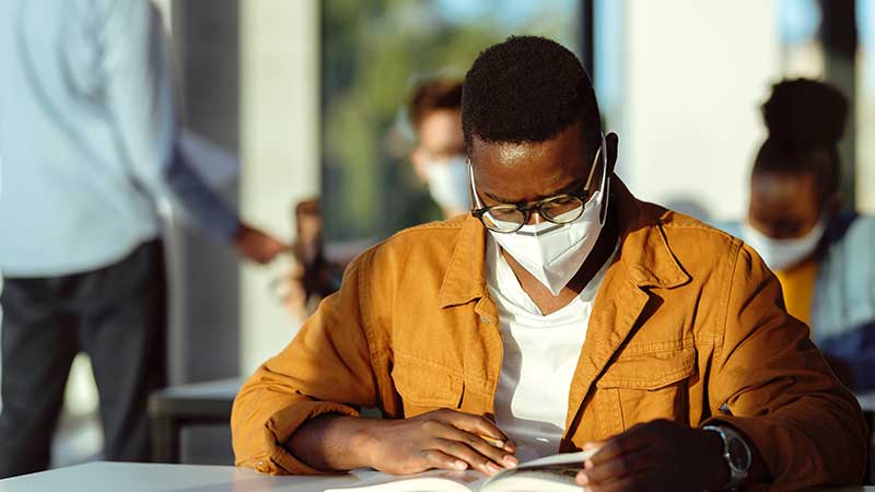 Black student reading and wearing COVID mask.