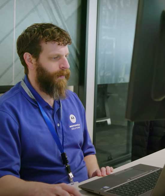 Software enginner in blue company shirt with lanyard working at a computer workstation.