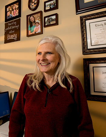 Lisa Villearreal smiling in front a wall on which her multiple diplomas hang.