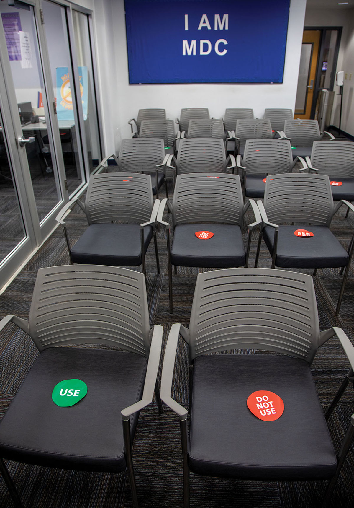 Advising room in a time of COVID shows chairs marked "Use" and "Do Not Use." The phrase "I Am MDC" is on the wall on a felt board.