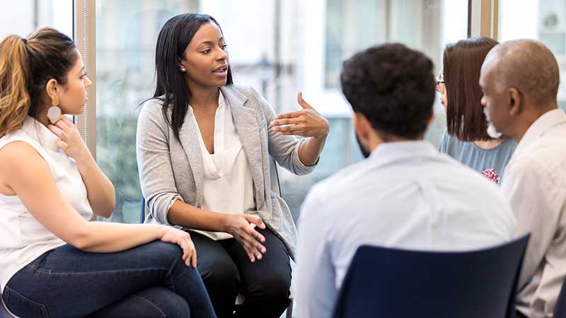 Black woman leading a roundtable discussion.