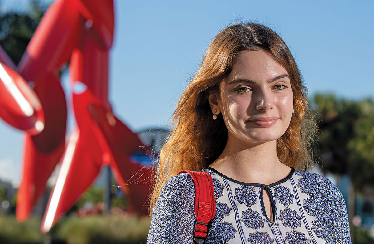 Daniela Figueroa outdoors with a giant red campus art sculpture behind her.