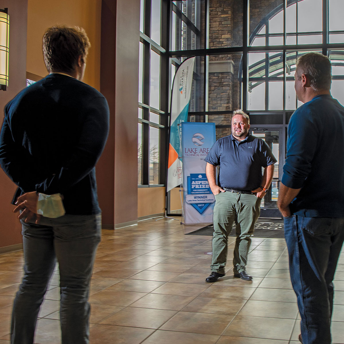 Three men chat in a large, open atrium.