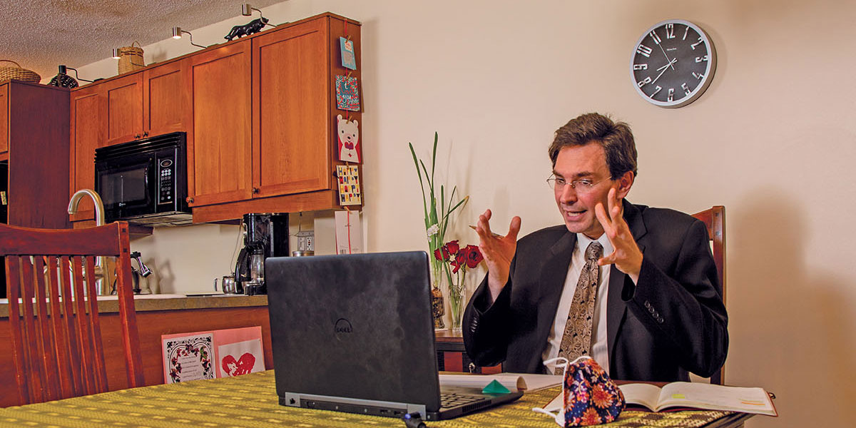 Assistant professor Nicolas Simon gesticulating at his laptop seated at his kitchen table.