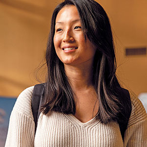 Asian woman in sweater, wearing backpack, smiling.