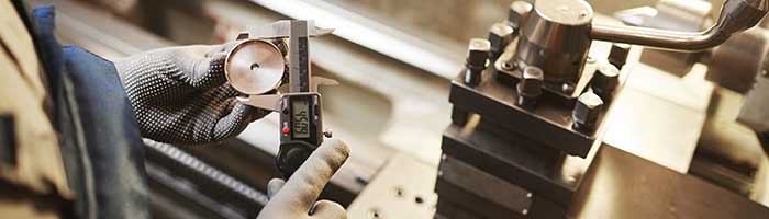 A technician measures a machined piece of round brass with calipers.