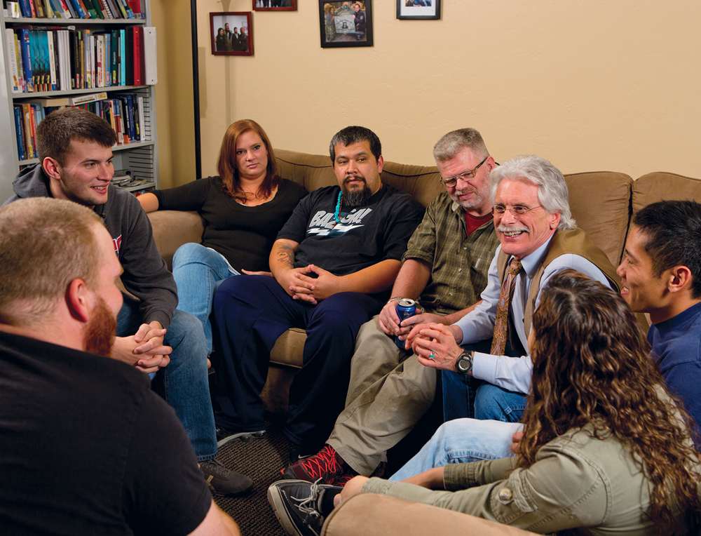 Eight people seated around living room furniture.