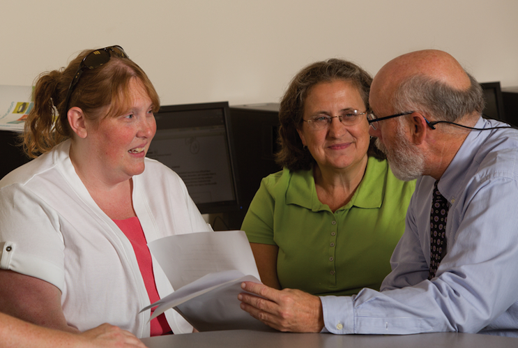 Candid shot of 3 adults talking over a handful of papers.