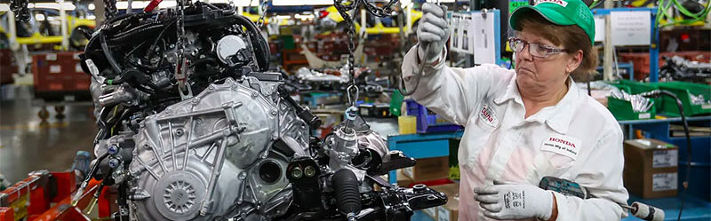 A female floor worker inspects an automotive engine at an Indiana car plant.