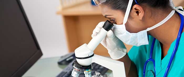 COVID-masked woman peers into a microscope.