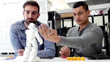 Two men work with a small tabletop robot unit.