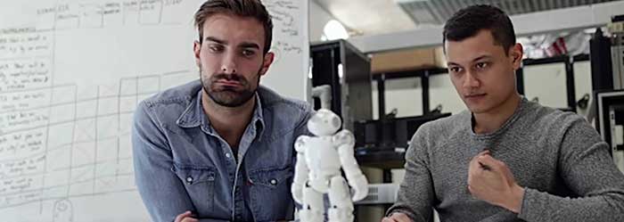 Two men work with a small tabletop robot unit.