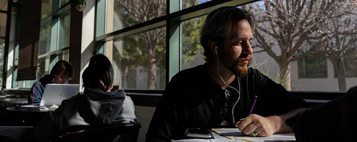 Student Zaq Woodward studies in a common area at a table in front of a window.