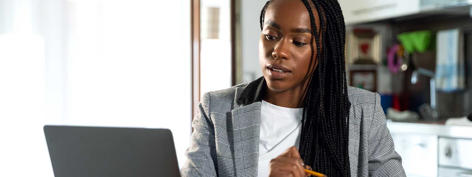 A professional Black woman working at a laptop in her kitchen.