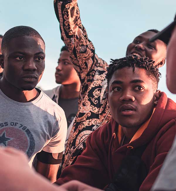 A gathering of several people. Two Black men are engaged in a conversation with a white guy in the foreground.