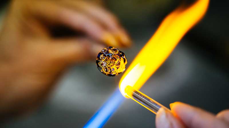 Glass artist melts a glass rod with a torch.