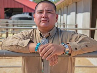 Navajo student Triston Black stands behind a livestock fence facing the camera.
