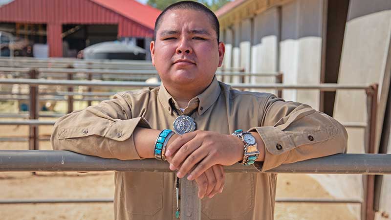 Navajo student Triston Black stands behind a livestock fence facing the camera.