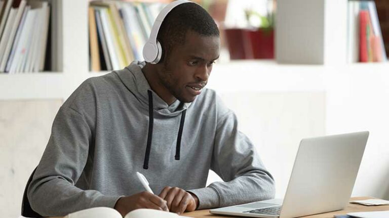 Young Black man taking notes and studying at a laptop.