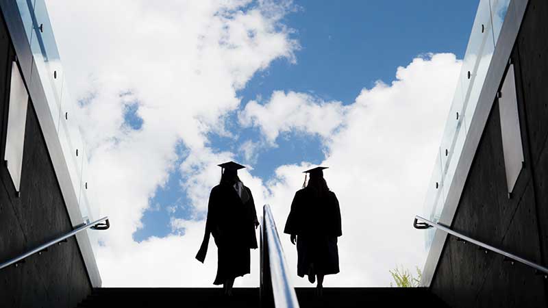 Two graduates walking up stairs in cap and gown.