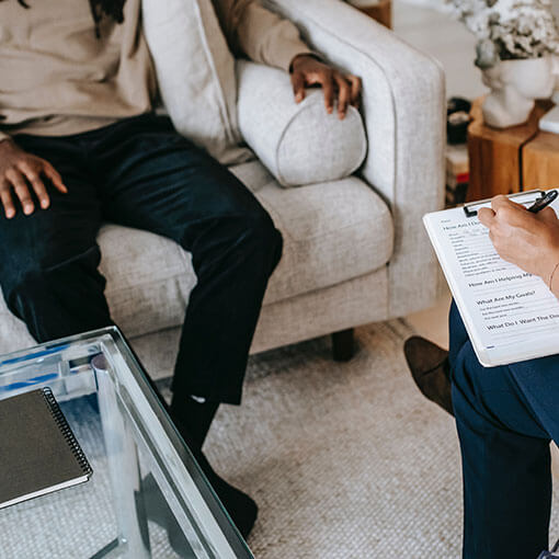 Faceless psychiatry patient talking while a therapist takes notes on couches.