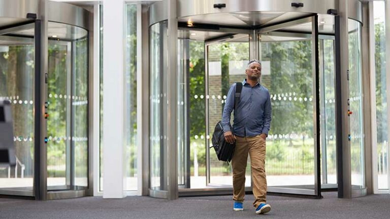 This dude's looking confident AF walking through revolving glass doors, carrying a couriers bag and blue shoes that match his shirt.