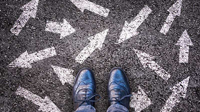 Looking down at a pair of shoes with chalk arrows drawn in various directions on the concrete below.