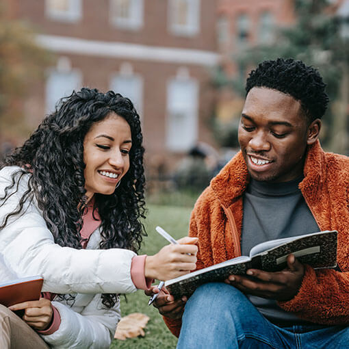 Two students sharing a book outdoors on campus.