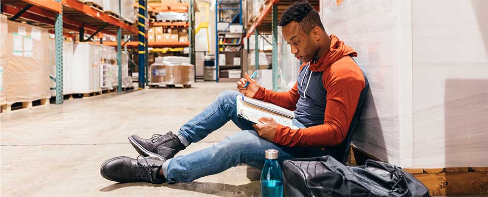 Young Black male studying in a work or warehouse environment.