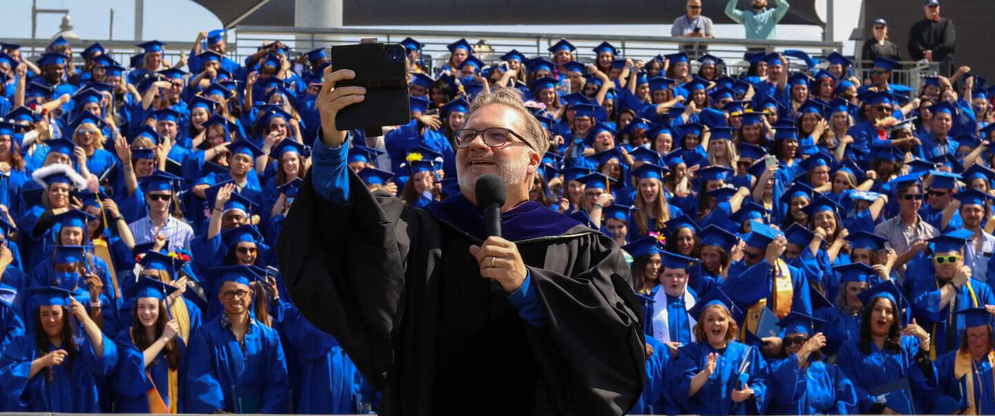 Amarillo College graduation celebration shows college president taking a selfie with graduating class.