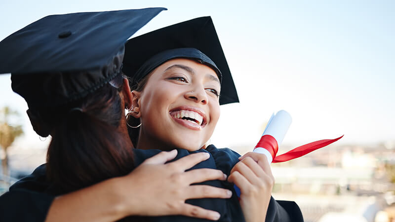 Graduates holding diplomas celebrate with a hug.