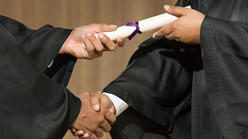 A simultaneous diploma handover with handshake. Four disembodied hands are in action.