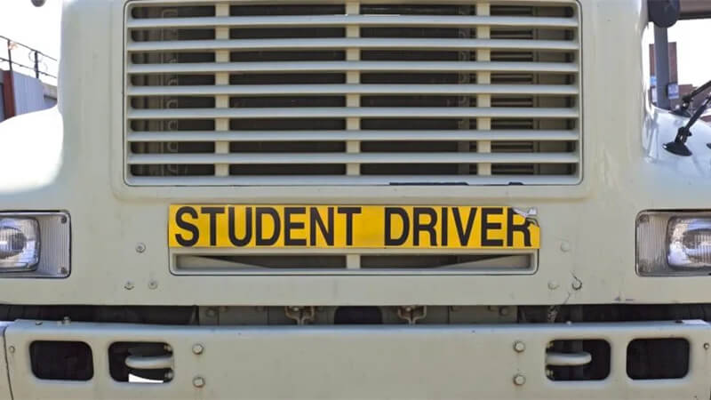 Big rig tractor displays yellow sign on front: Student Driver.