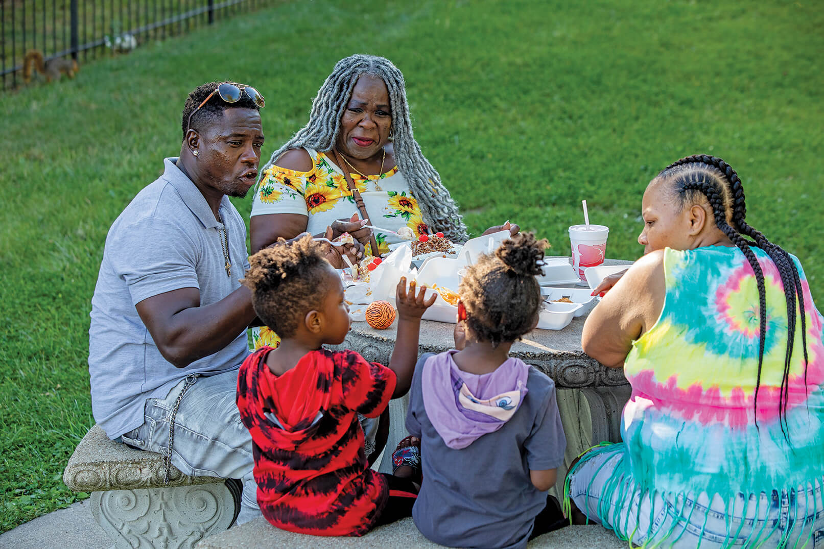 Family eats outdoors on a concrete picnic table.