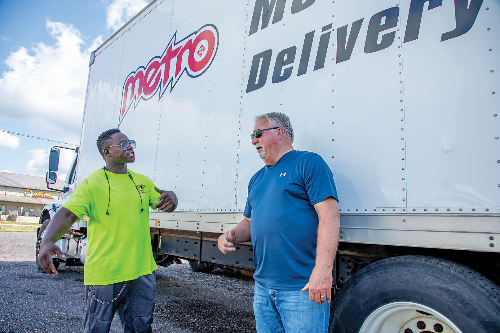 Two men talk along side a delivery truck.