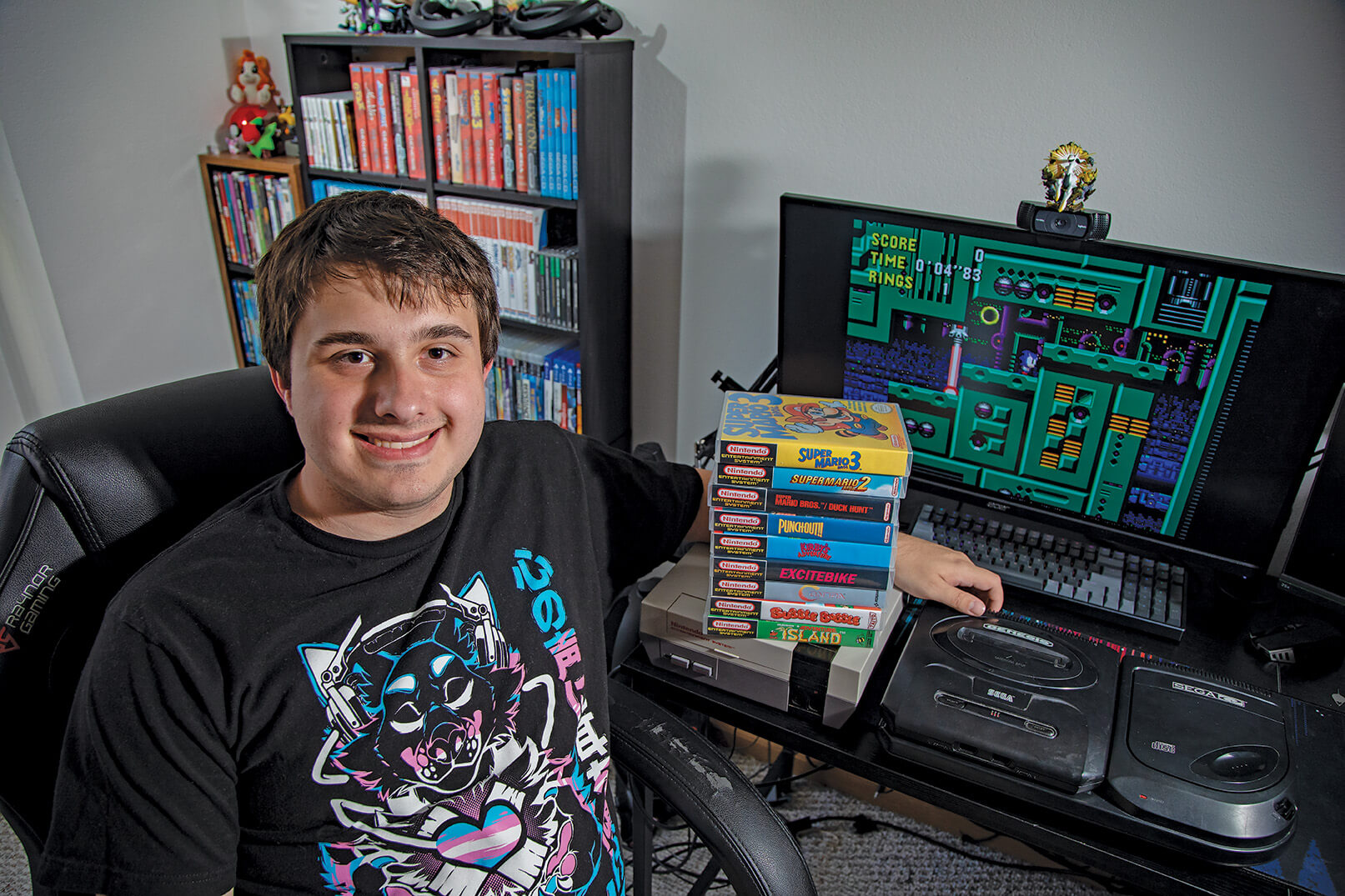 Young dude with a stack of boxed SNES games on his desk. A computer screen running Super Mario World is in the background.