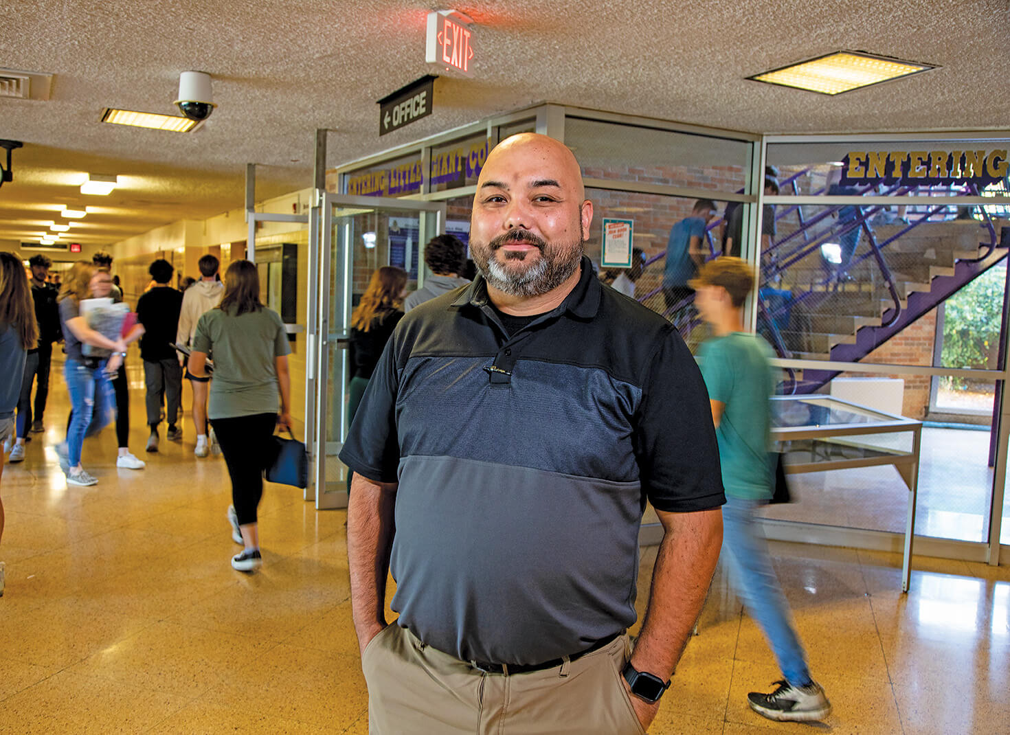 Man standing in school hallway with students milling about behind him.