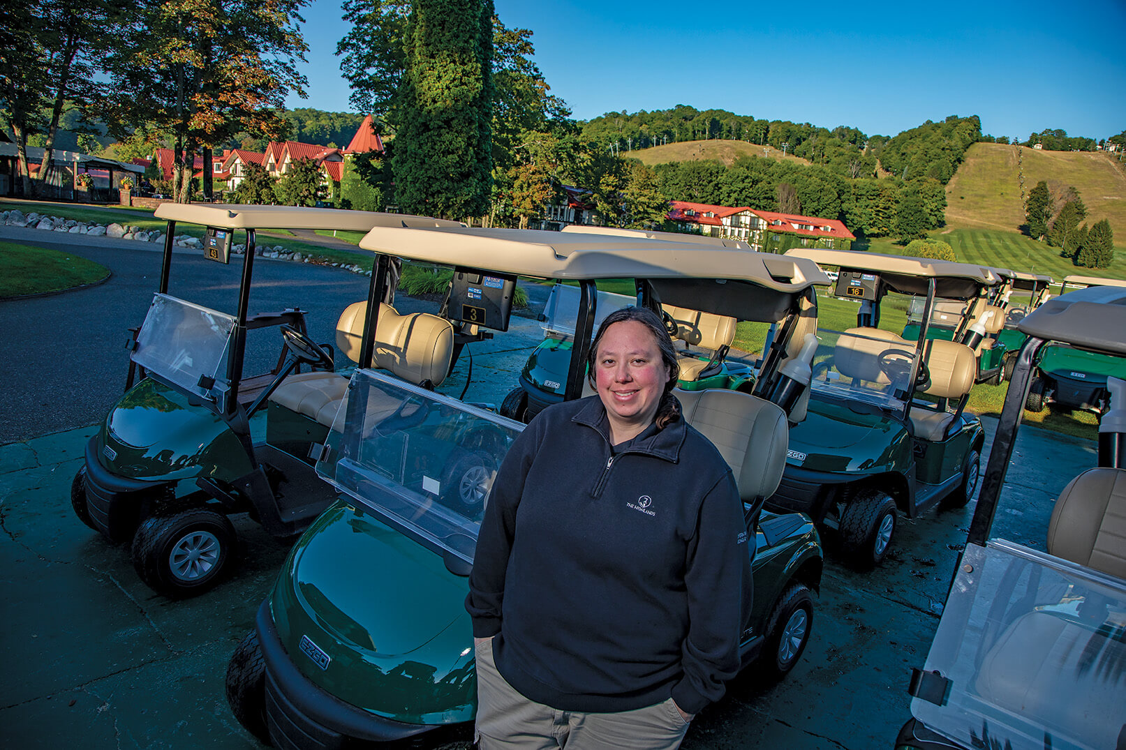 Woman stands before fleet of shiny, forest-green golf carts.