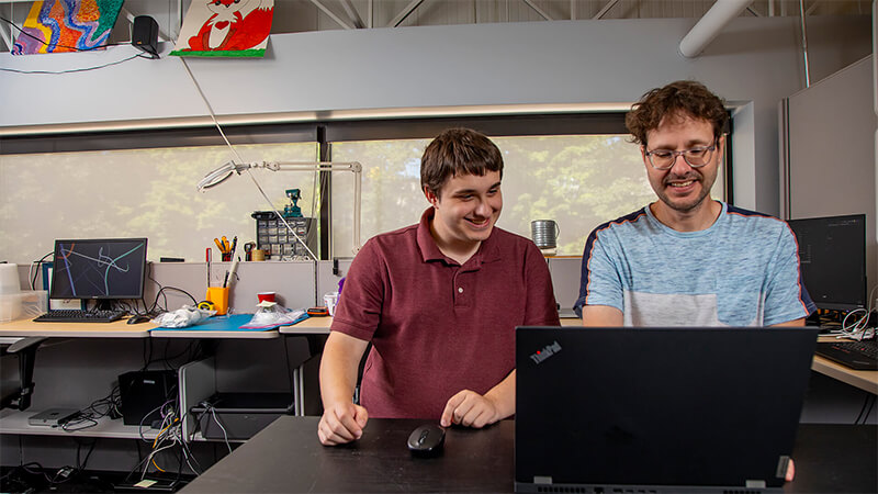 Two guys looking at a laptop screen at a standing desk.
