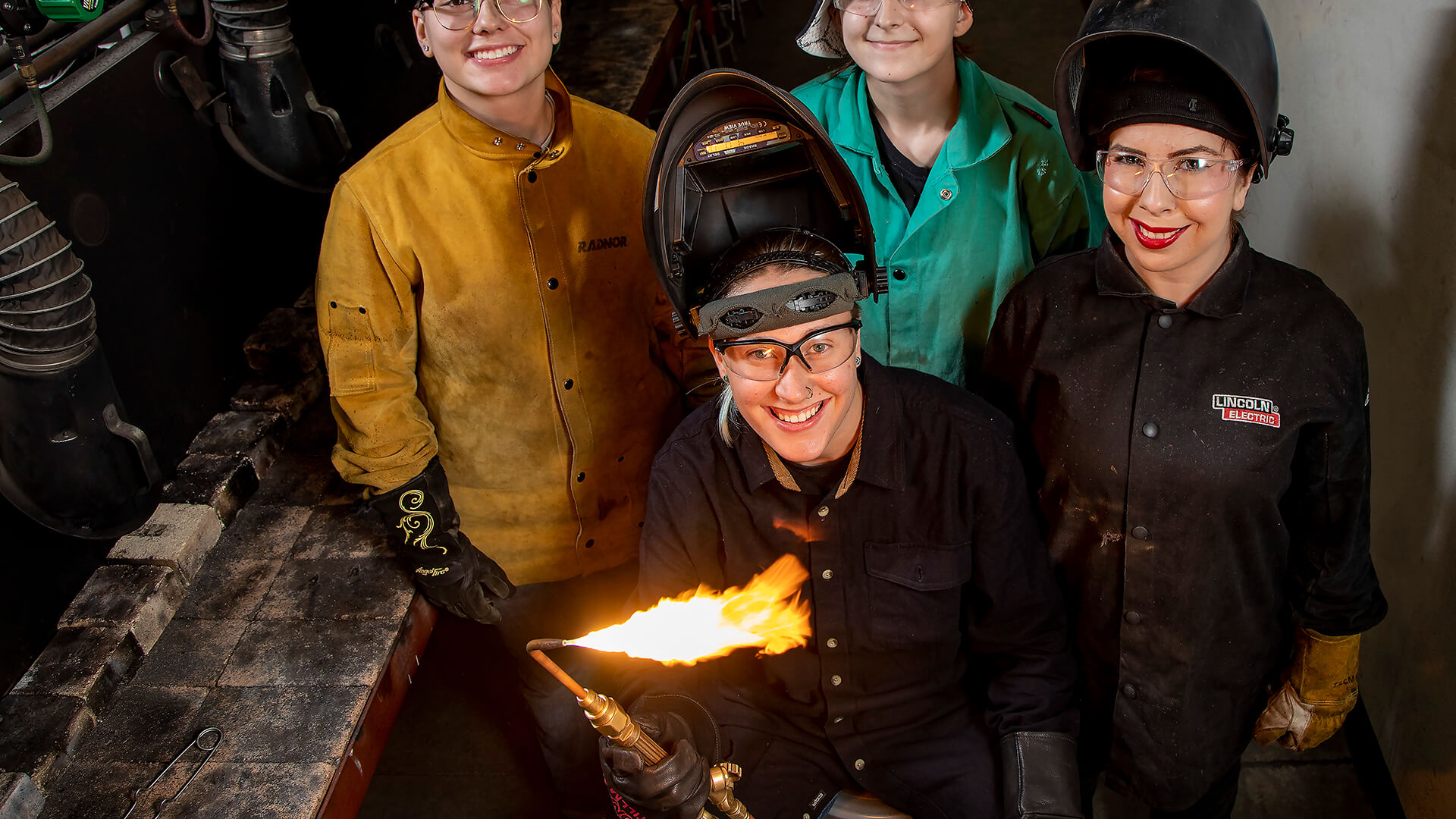 Cat Beaver, flaming torch in hand, is surrounded by female classmates in her welding program at Victor Valley College