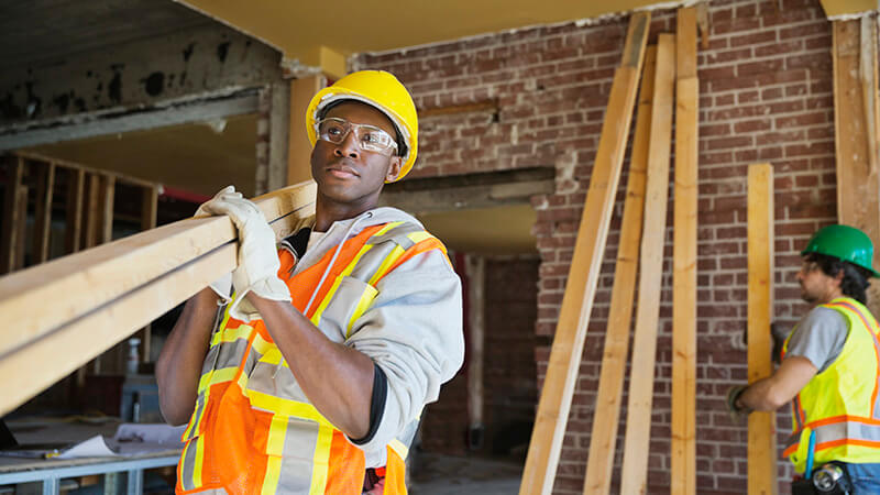 Tradesmen carrying lumber at construction site stock photo